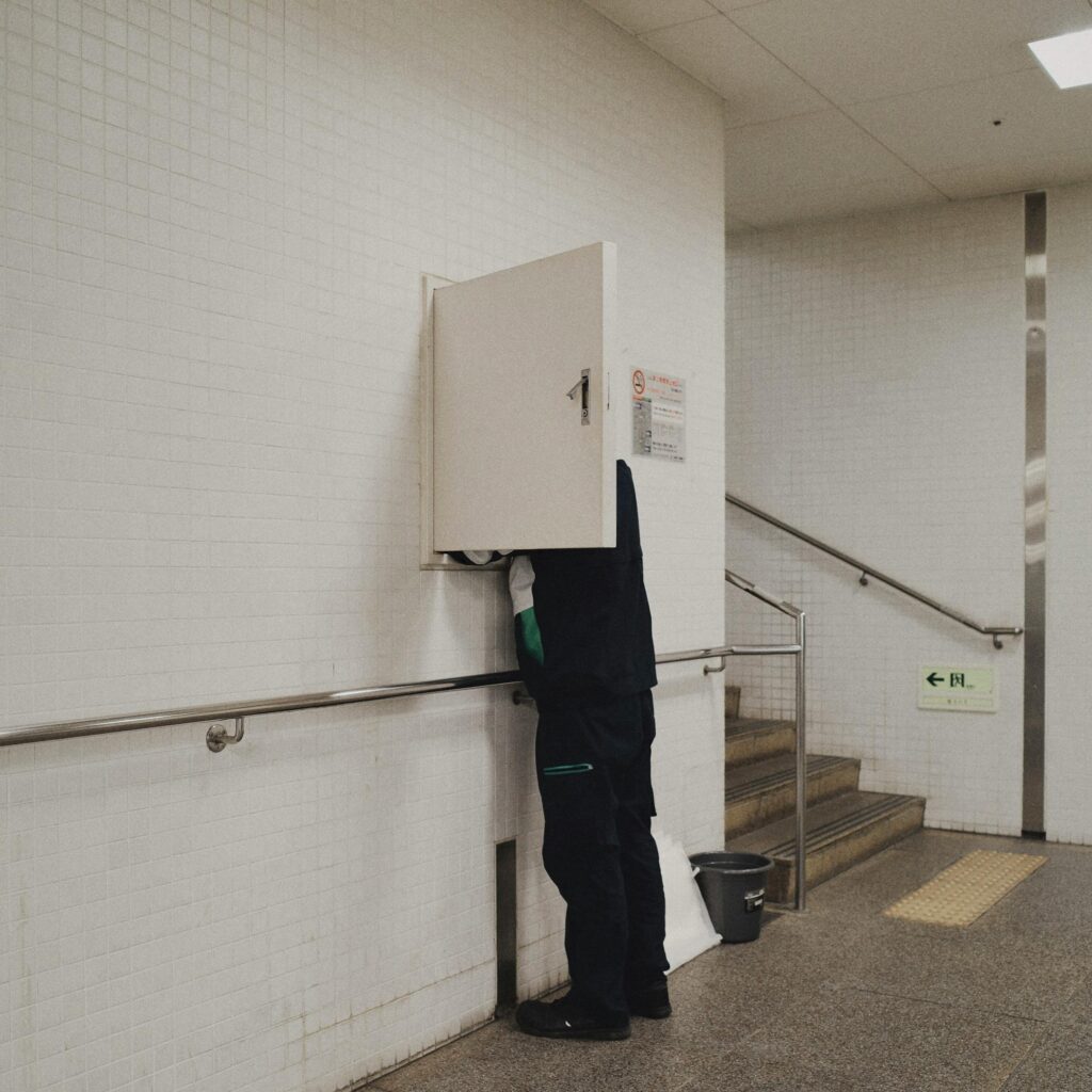 Maintenance worker opening a wall panel in an indoor hallway with white tiles.